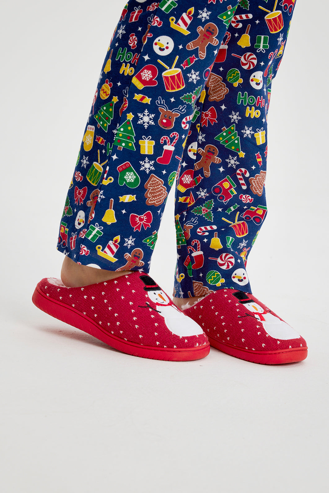 Une paire de jambes portant des chaussons de Noël rouges fantaisie avec un bonhomme de neige dessus.
